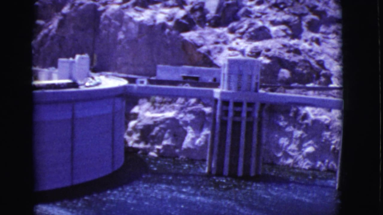 Dam model with concrete tower, curved wall, water, and rocky backdrop.