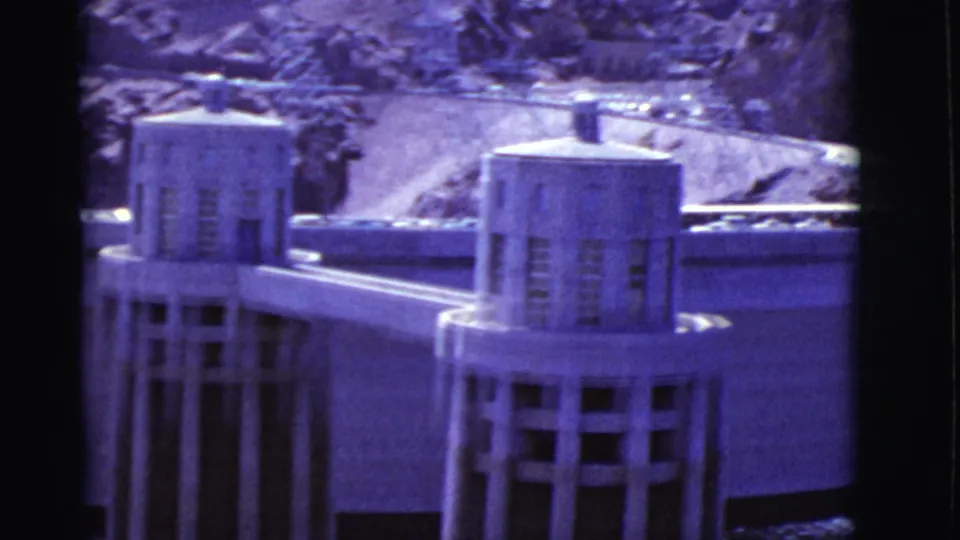 1968 8mm frame showing two tower structures and the curved dam model wall, with strong purple color shift and soft focus.