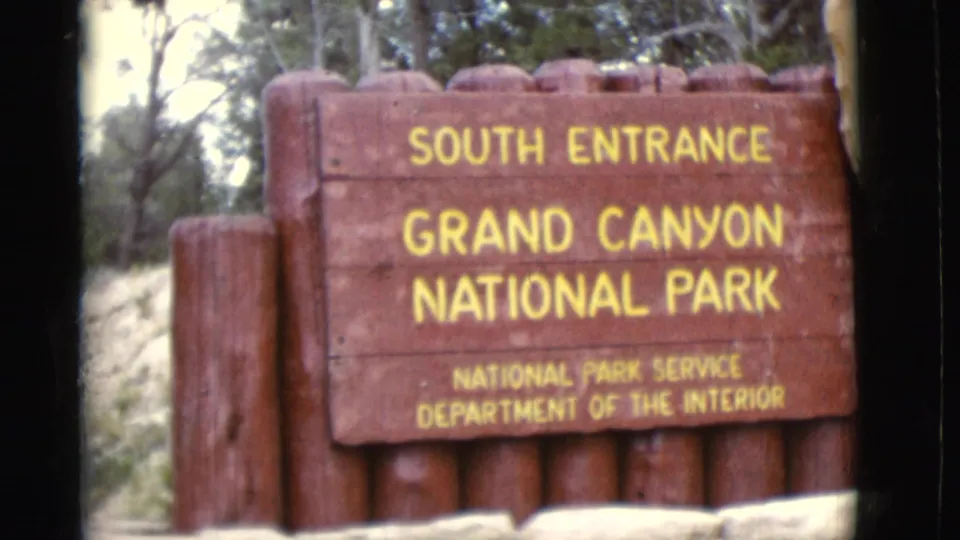 1968 Arizona home-movie frame of the South Entrance Grand Canyon National Park sign with National Park Service text visible.