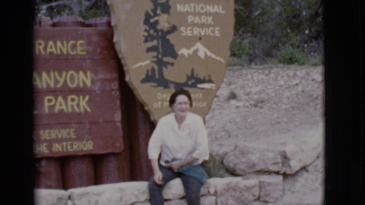 Woman smiles while seated in front of a National Park Service sign and wooden entrance marker.