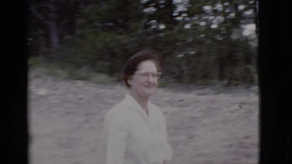 The woman appears in profile while walking through a wooded Arizona park setting in 1968 8mm home-movie footage.