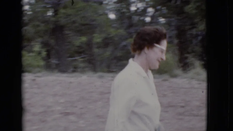 A closer side view shows the woman in glasses and a light blouse walking through the wooded Arizona location.