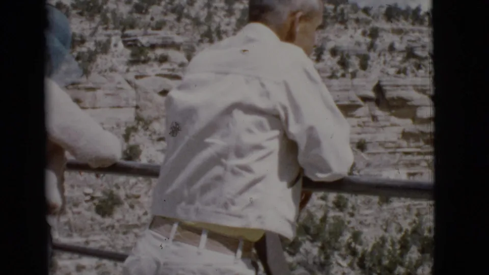 1968 Arizona 8mm frame showing a rear view of a man leaning on a railing at a rocky canyon overlook.