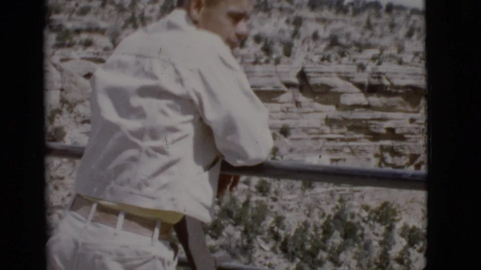 1968 Arizona home-movie frame of a man standing at a railing with layered canyon terrain in the background.