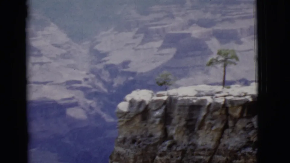 1968 Arizona home-movie frame of a rocky Grand Canyon rim with a small tree and soft, distant canyon strata.