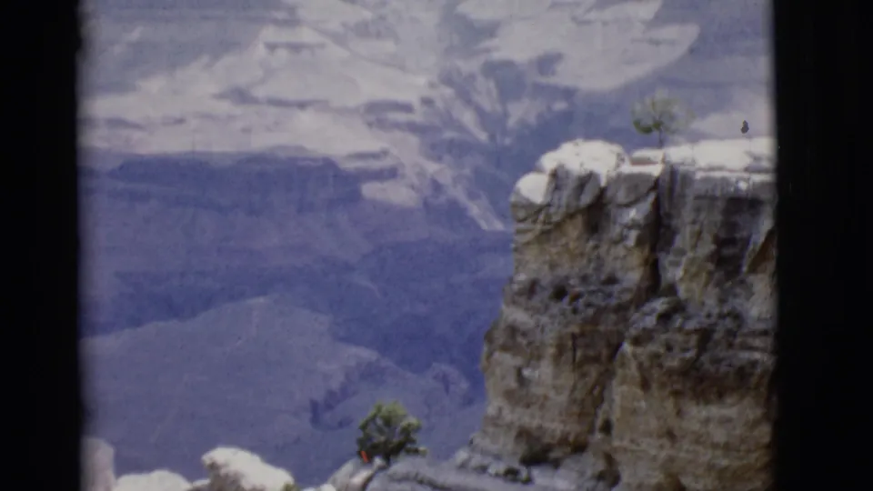 1968 Arizona 8mm frame with a tall rock outcrop, distant canyon wall, and sparse trees along the overlook edge.