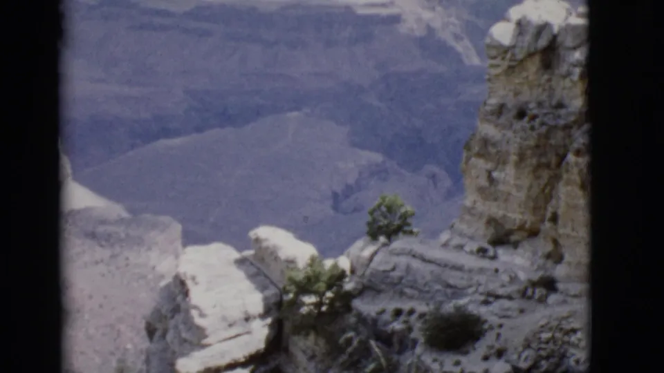 1968 Arizona 8mm frame showing foreground rock ledges, sparse trees, and a distant canyon wall across the ravine.