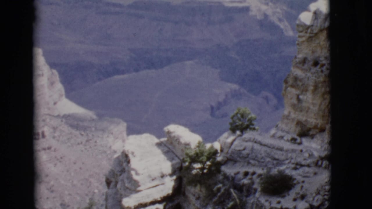 Snow-dusted canyon cliffs and sparse trees seen from above on soft 8mm footage.