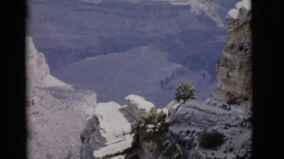 1968 Arizona 8mm view of pale canyon ledges, a small tree, and distant blue canyon walls from an elevated or aerial perspective.