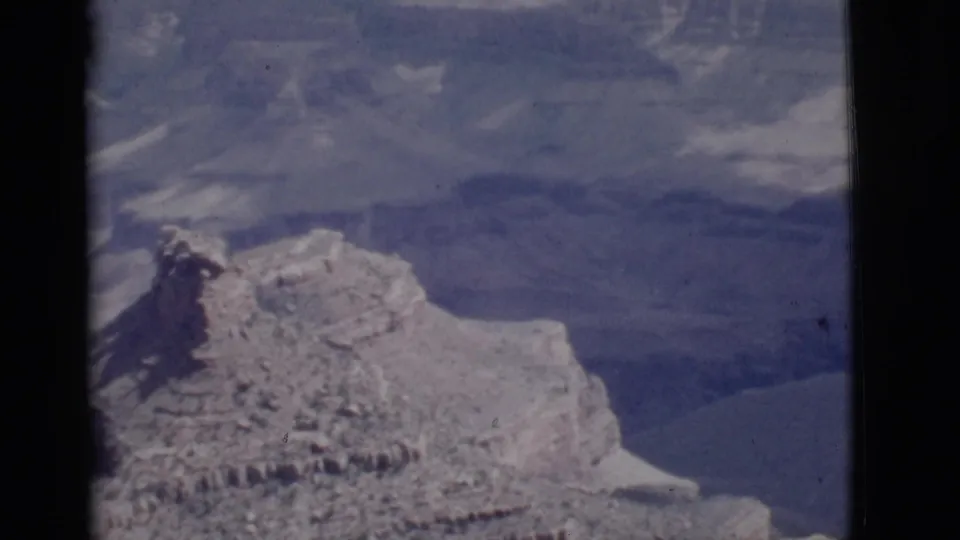 1968 Arizona 8mm frame of a rugged canyon ridge with light snow, layered rock, and distant shadowed canyon walls.