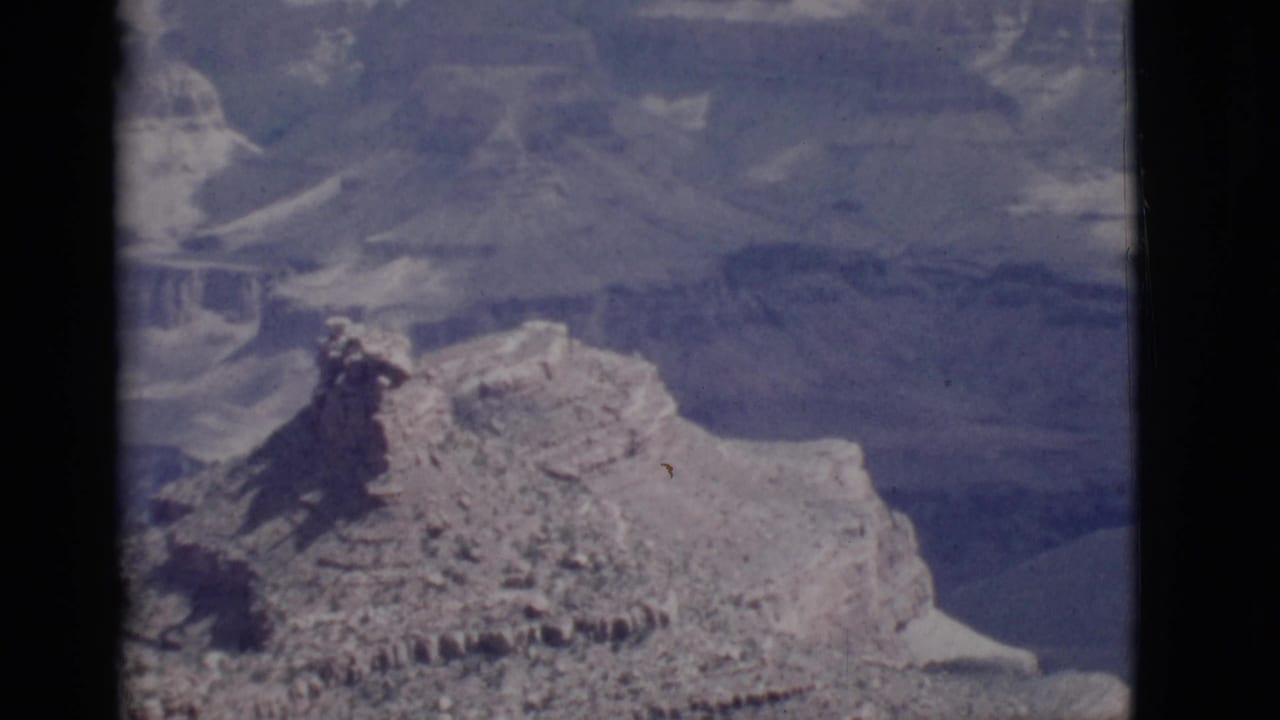 Wide view of layered canyon rock formations seen through a dark 8mm film frame.