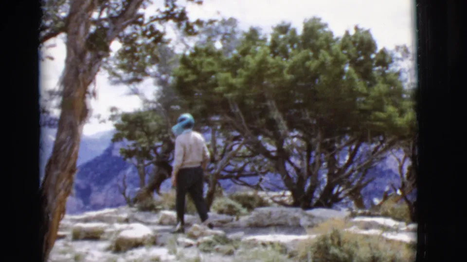 In 1968 Arizona footage, a person in a light shirt and dark pants walks away through rocks and desert trees.