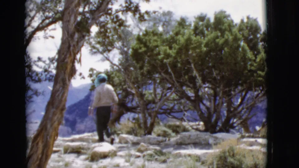 The walker continues across rocky Arizona terrain, framed by trees and distant hills in the 8mm home-movie shot.