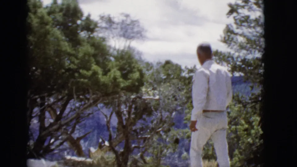 At the end of the clip, the man appears farther from the camera on an Arizona overlook, with trees and canyon landscape behind him.