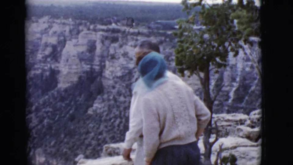 1968 Arizona home-movie frame of two tourists near a canyon rim, with the woman in a blue headscarf facing the view.
