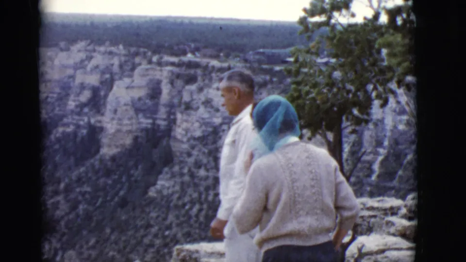 At the canyon overlook, the man briefly turns in profile while the woman remains near the rocky rim in 1968 Arizona travel footage.