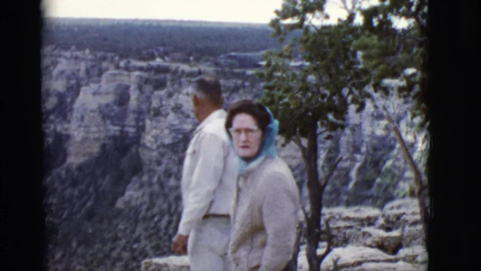 1968 Arizona home-movie frame of an adult couple near the Grand Canyon rim, with the woman in a blue headscarf facing the camera.