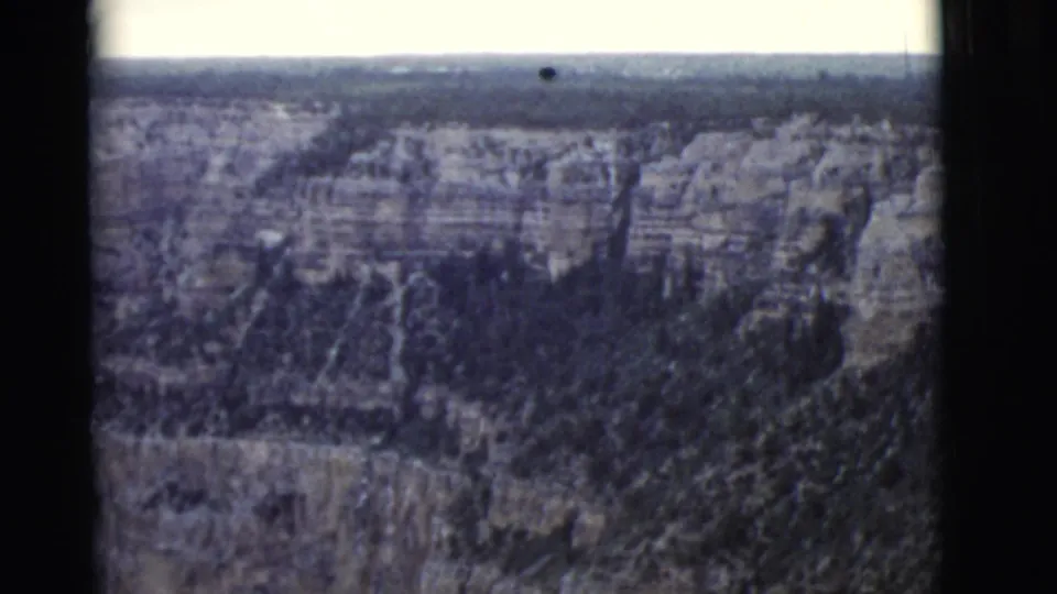 1968 8mm aerial view over Arizona canyon walls with dark forest below and visible film-frame borders.