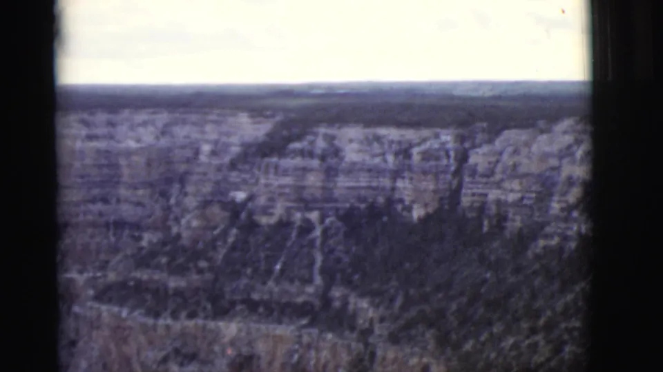 Aerial home-movie frame showing Arizona canyon strata, dark ravines, and a hazy distant horizon.