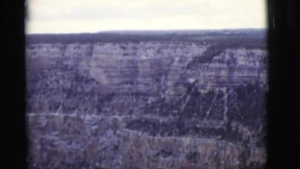 1968 8mm frame of an Arizona canyon rim, steep wooded terrain, and softened rock layers seen from above.