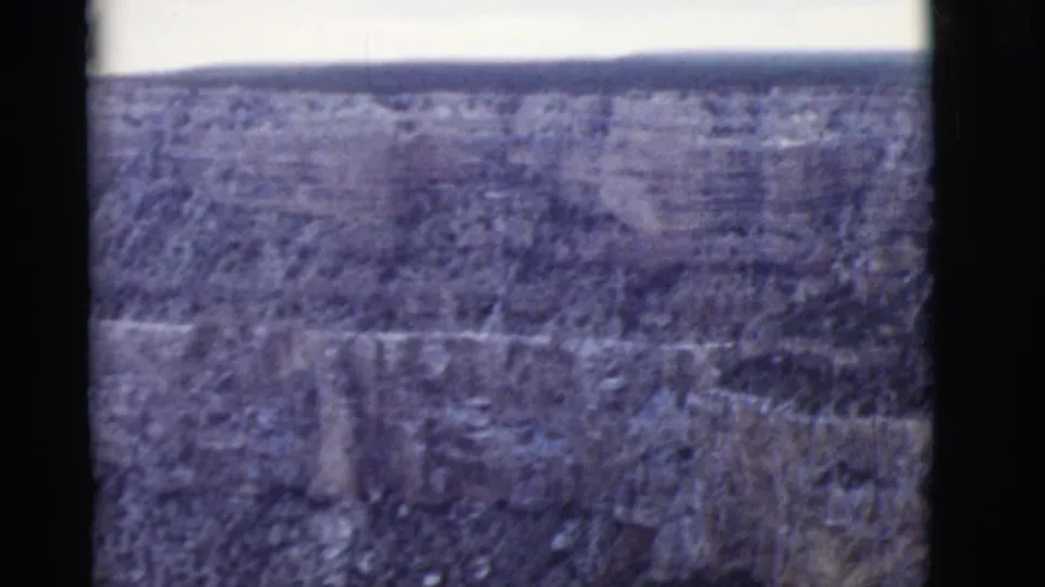 Vintage 8mm aerial view of Arizona canyon walls, exposed strata, scattered dark vegetation, and faded color.