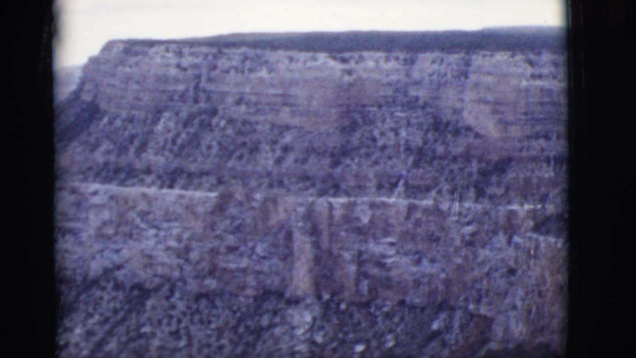 Layered canyon wall and mesa under a pale sky with dark film borders.