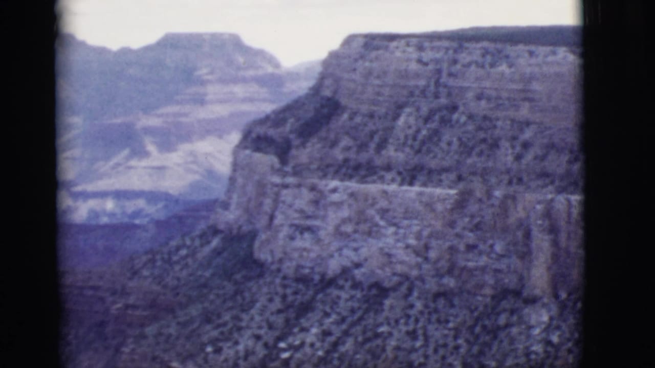 1968 Arizona landscape frame with steep canyon walls, a distant mesa, hazy ridgelines, and visible 8mm frame edges.
