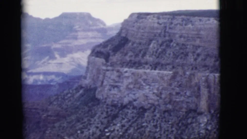 1968 Arizona landscape frame with steep canyon walls, a distant mesa, hazy ridgelines, and visible 8mm frame edges.