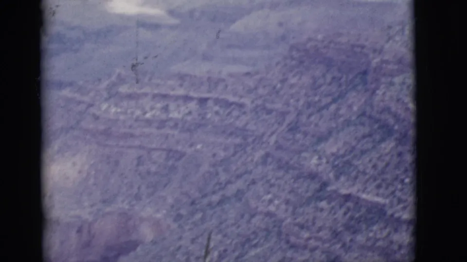 1968 Arizona 8mm frame showing a rocky canyon slope, faint horizontal strata, haze, and visible aging marks on the film.