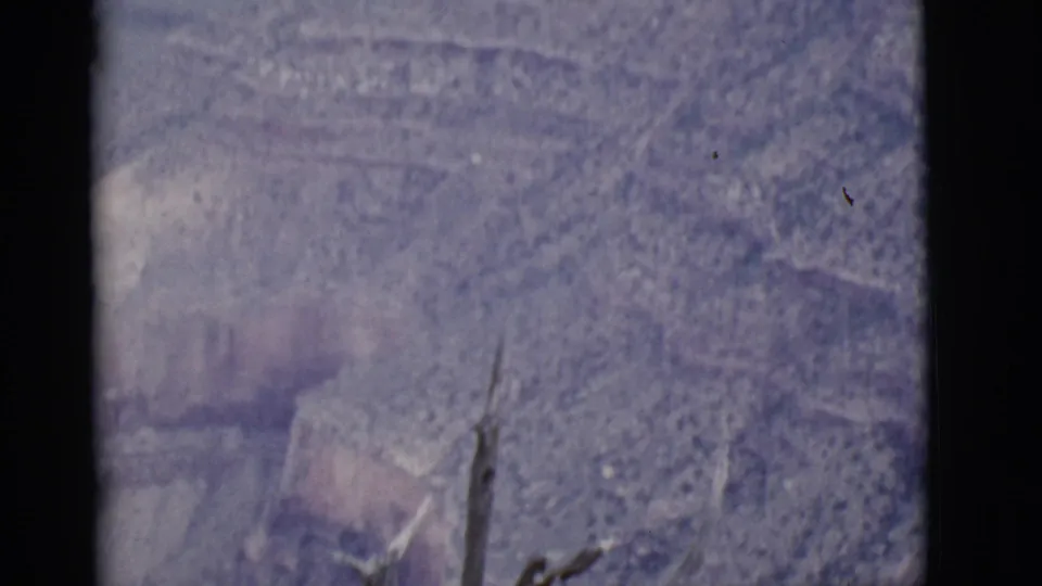 1968 8mm Arizona canyon view with muted layered cliffs, sparse brush, and dark frame edges from the film scan.