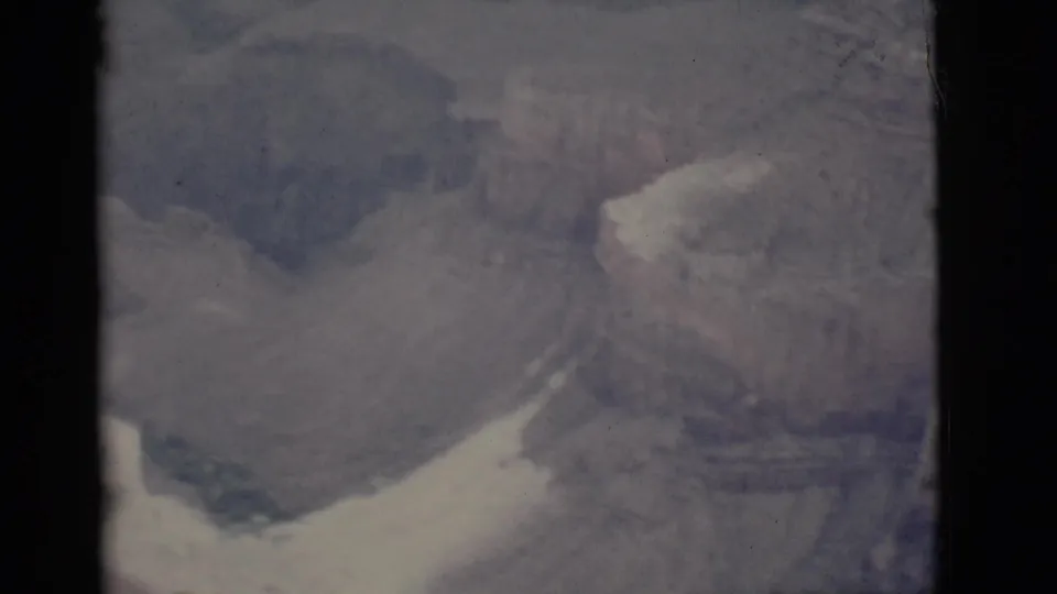 Muted 1968 Arizona canyon frame with distant layered cliffs, a pale slope, soft focus, and visible film border.