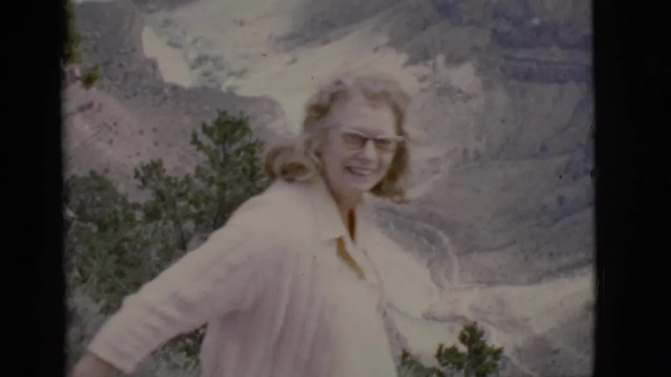 Woman in glasses and a light pink cardigan poses at an Arizona canyon overlook in 1968 home-movie footage.