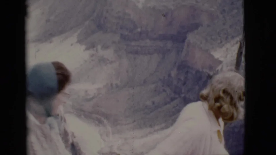 At a 1968 Arizona canyon overlook, a woman looks away from camera as a person in a blue hat appears beside her.