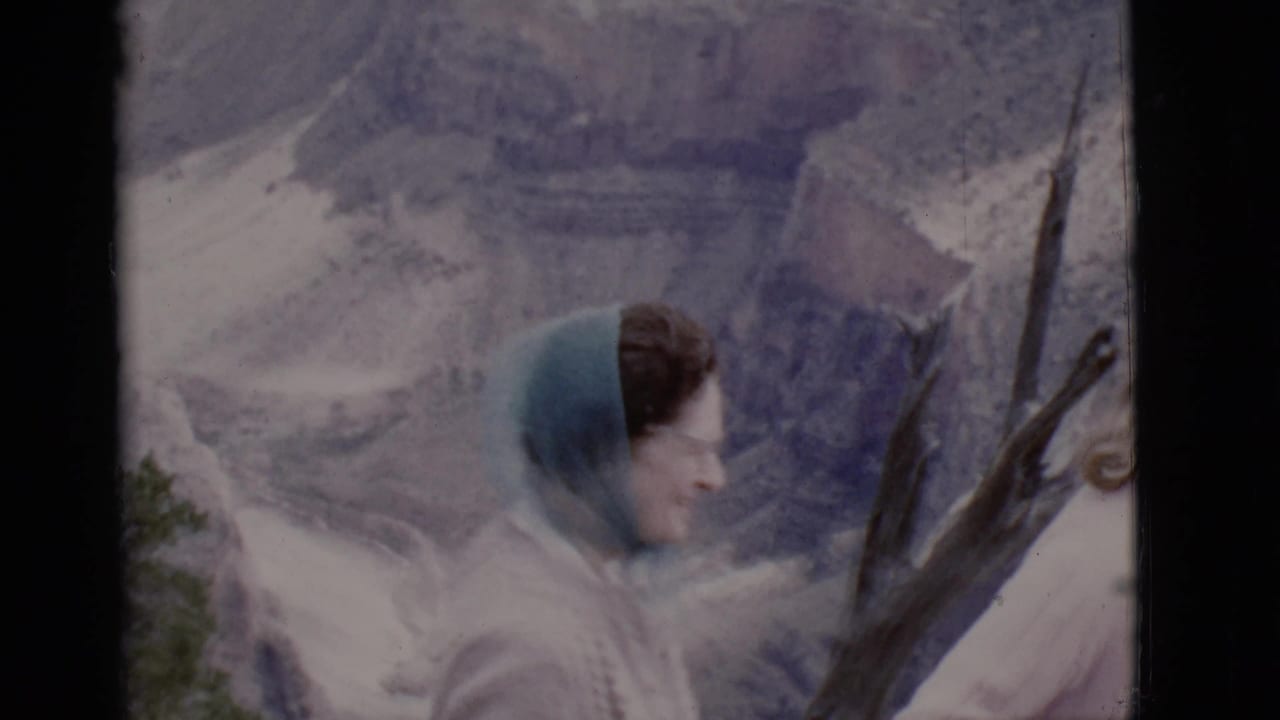 Two women near a rocky mountain overlook, one partly blurred beside bare branches.