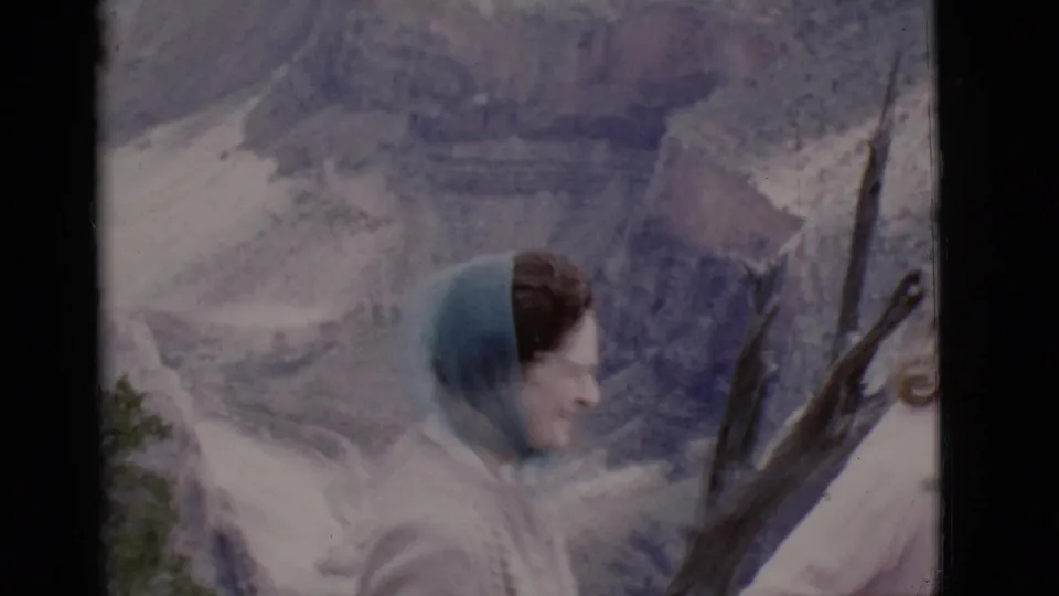 1968 Arizona home-movie frame showing two women at a mountain overlook, with a headscarf, pale sweaters, branches, and rocky terrain behind them.