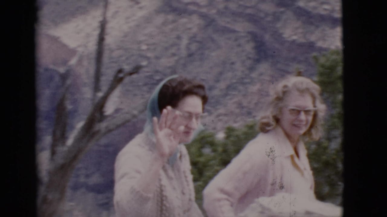 1968 Arizona travel frame with one woman waving to the camera and another smiling, both wearing glasses before a rocky mountain backdrop.