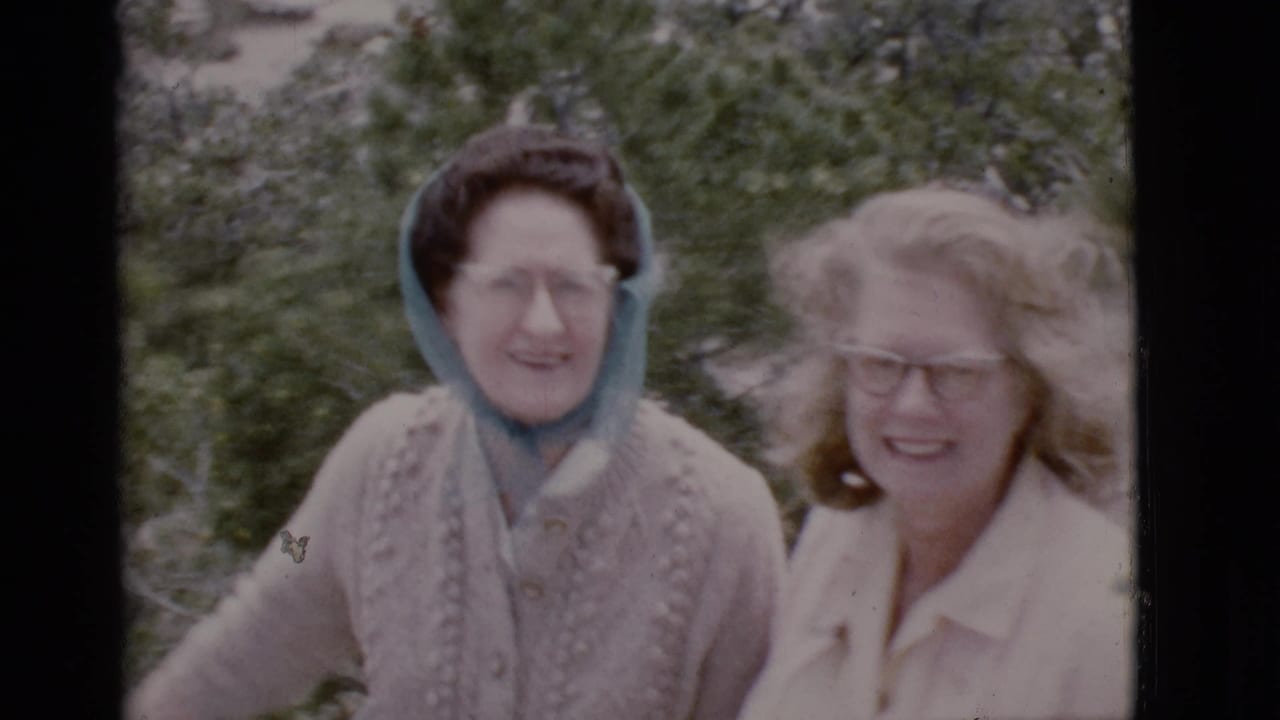 Two adult women smile outdoors near trees and canyon vegetation.