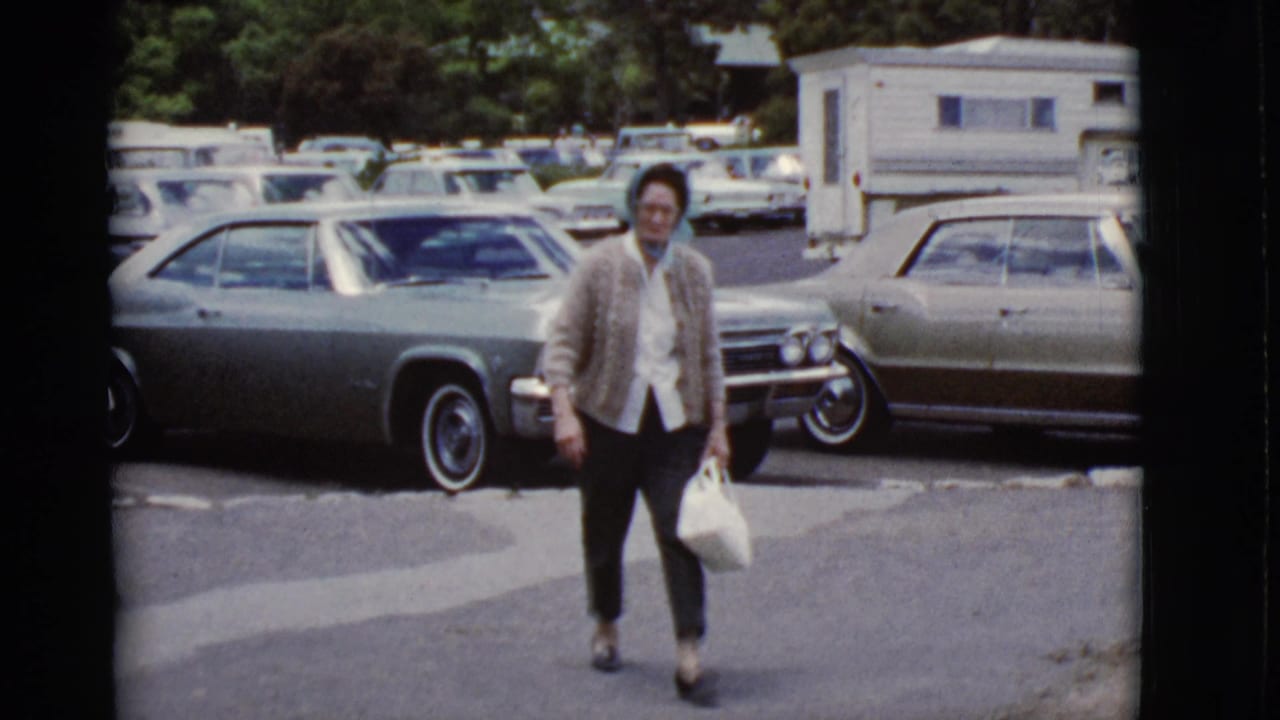 Woman in a headscarf walks across a parking lot carrying a white handbag.