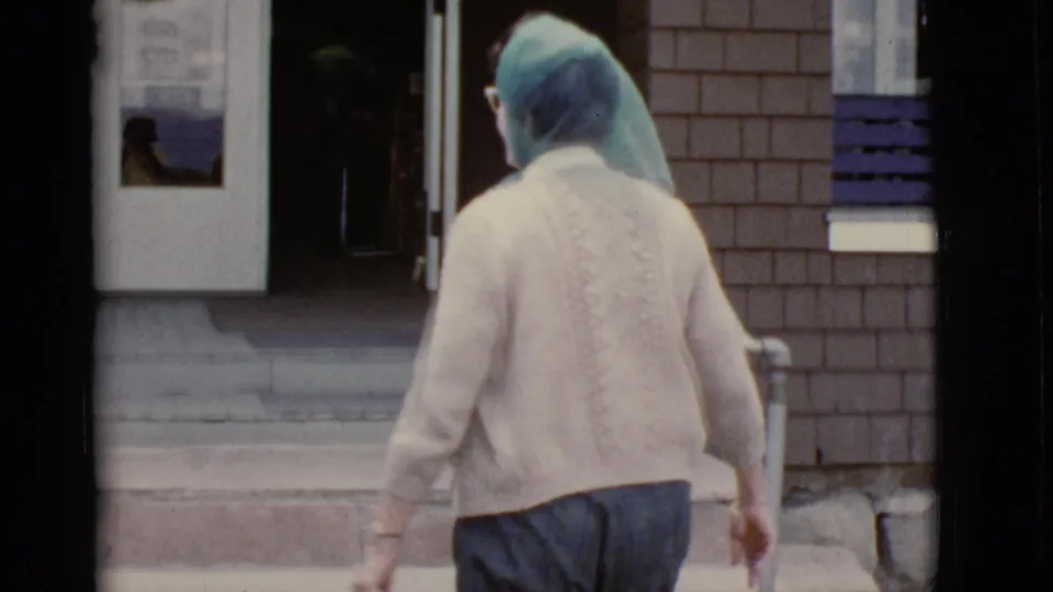 The woman, seen from behind in her headscarf and cardigan, approaches an open doorway of a brick building in the 1968 Arizona clip.