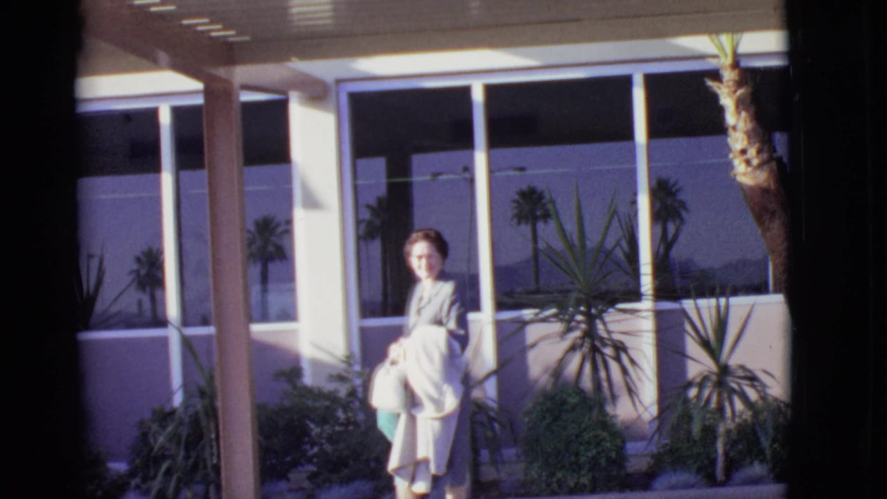 Woman holding shopping bags outside an airport terminal with palm landscaping.