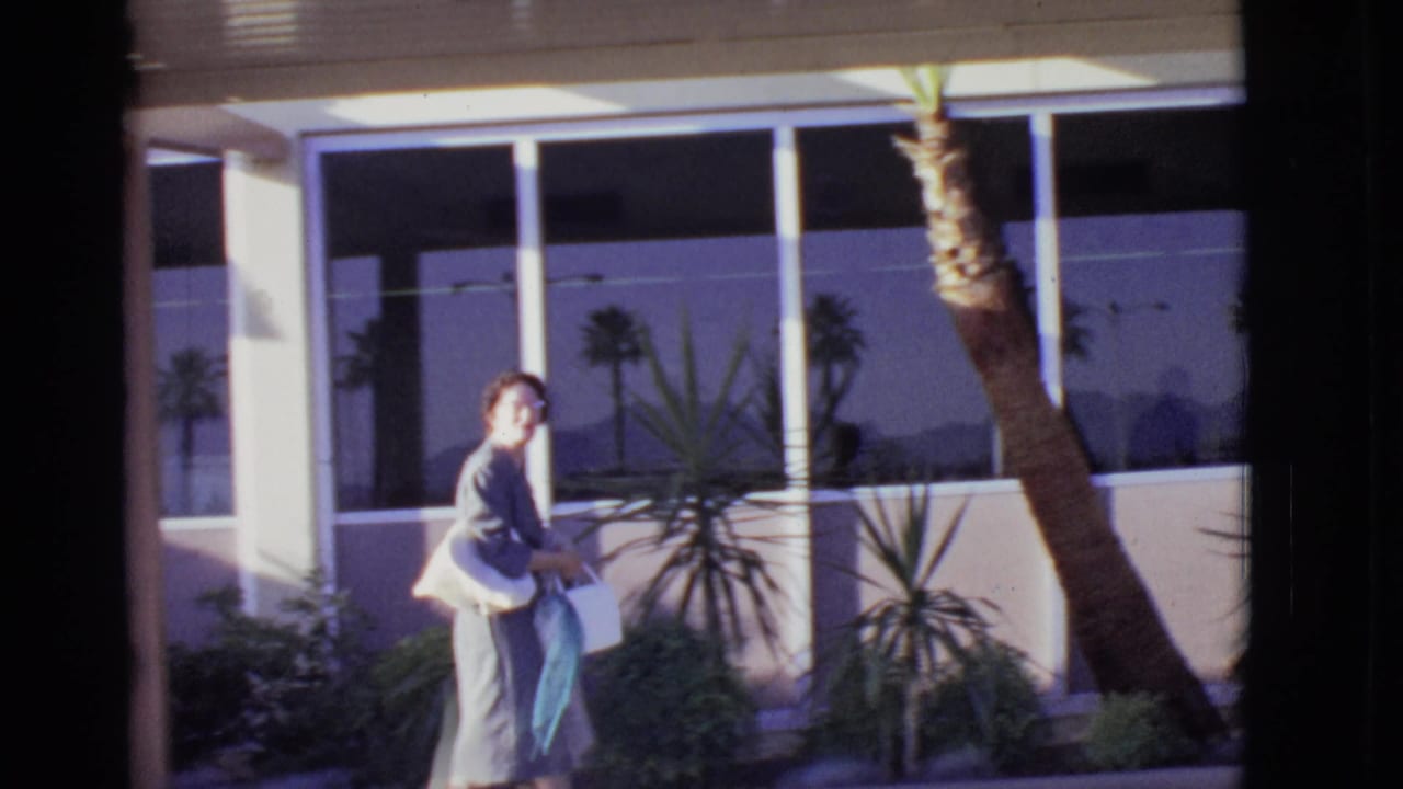 Woman turns near airport windows while holding bags and a purse.