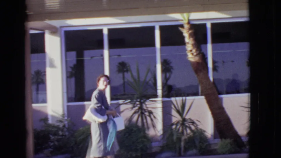 The woman turns beside the terminal landscaping, carrying shopping bags and a purse in the Arizona airport scene.