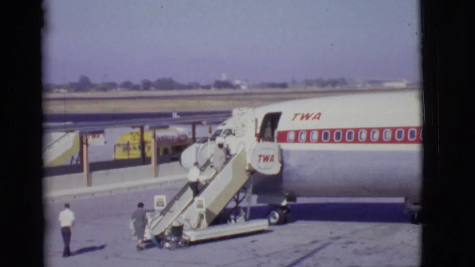 Passengers ascend mobile stairs to a TWA commercial aircraft on an open airport tarmac in the 1968 Arizona footage.