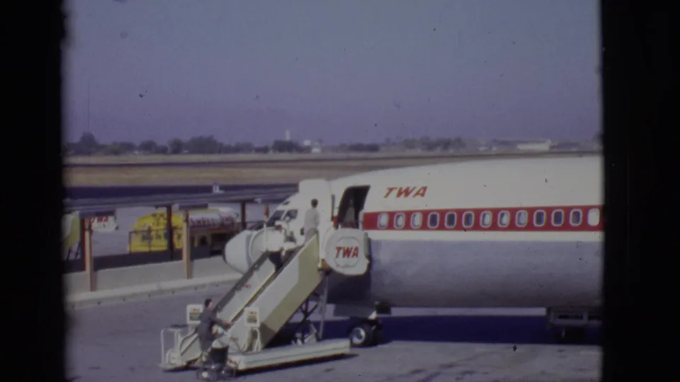 1968 Arizona airport scene showing passengers boarding a TWA airliner by mobile stairs, with ground equipment visible on the apron.
