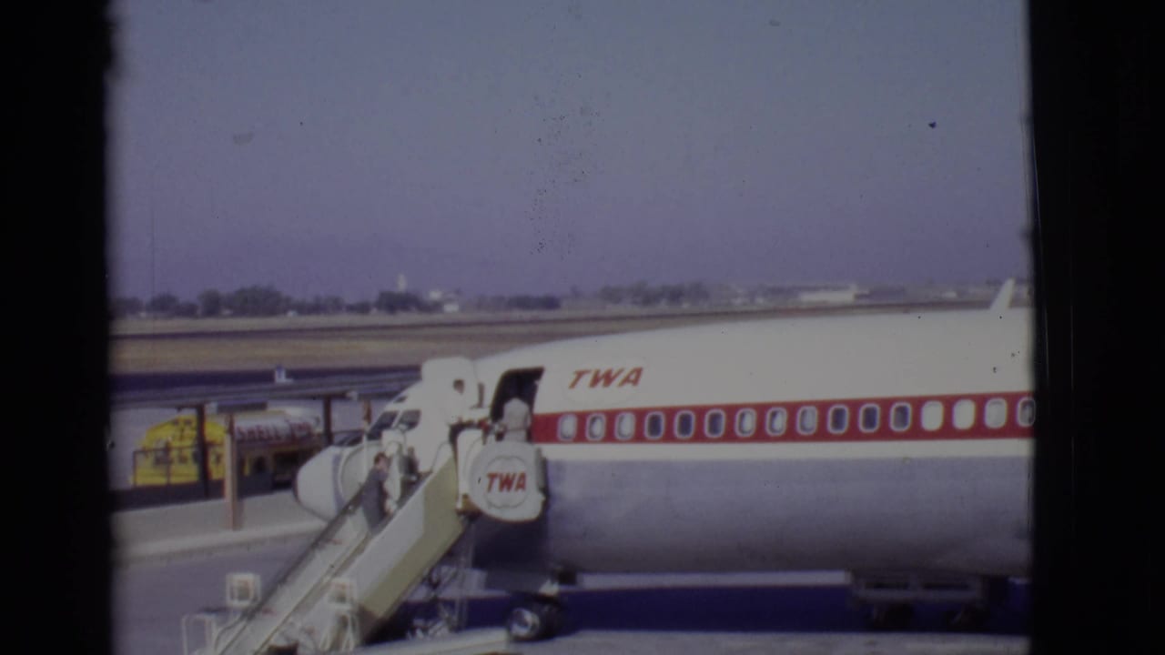 TWA passenger jet on an airport tarmac with mobile stairs at the open door.