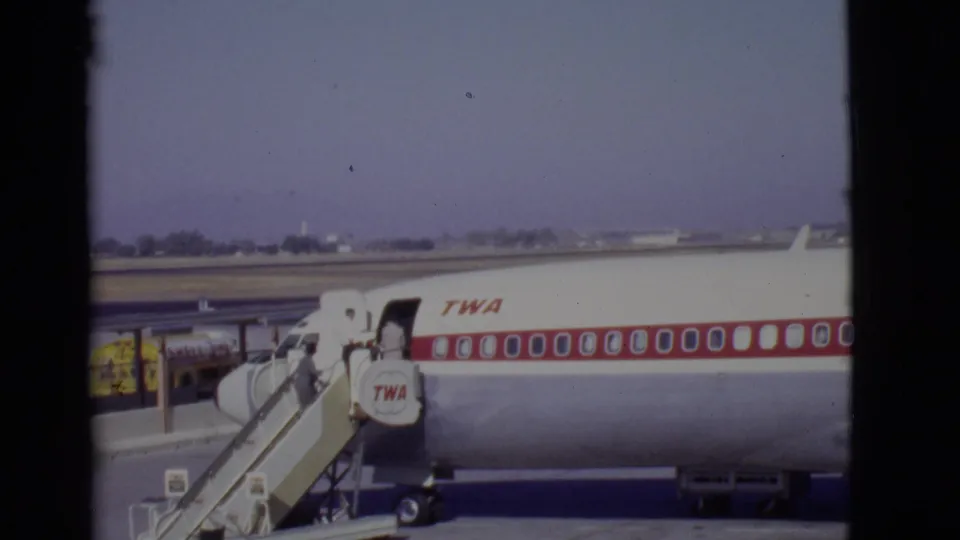A TWA passenger plane is parked on the Arizona tarmac while travelers board through the forward door.