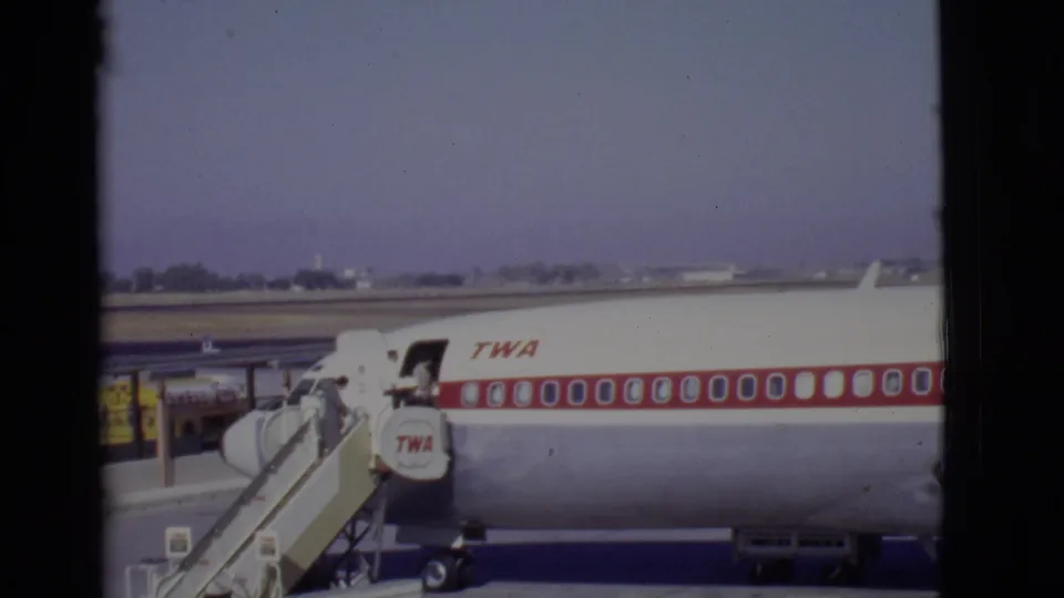 A white and red TWA aircraft remains parked on the Arizona apron as passengers board by mobile stairs.