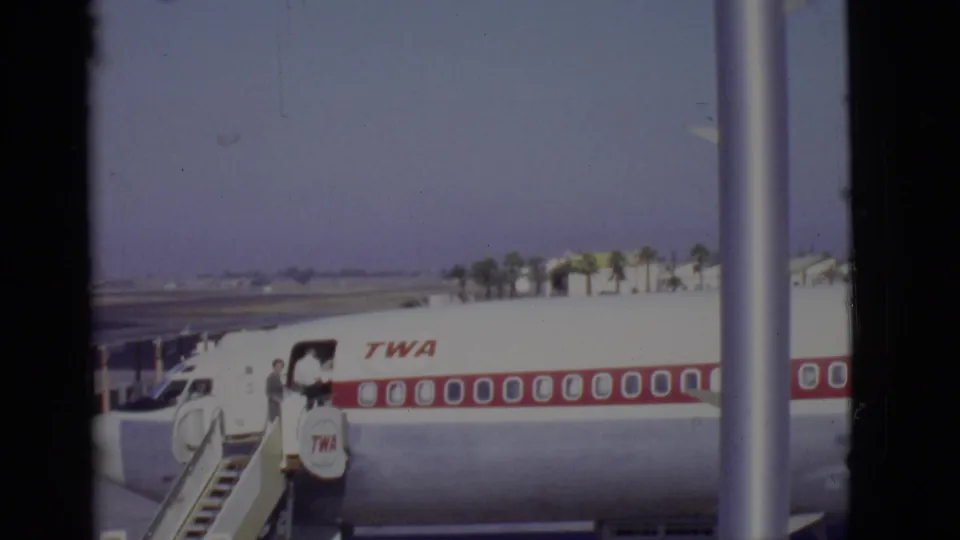 Arizona, 1968 home-movie frame of passengers boarding a white TWA aircraft with red stripe from mobile stairs on a sunny tarmac.