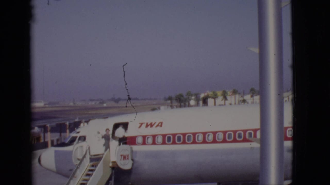 A TWA aircraft sits beside mobile stairs as passengers board on the tarmac.