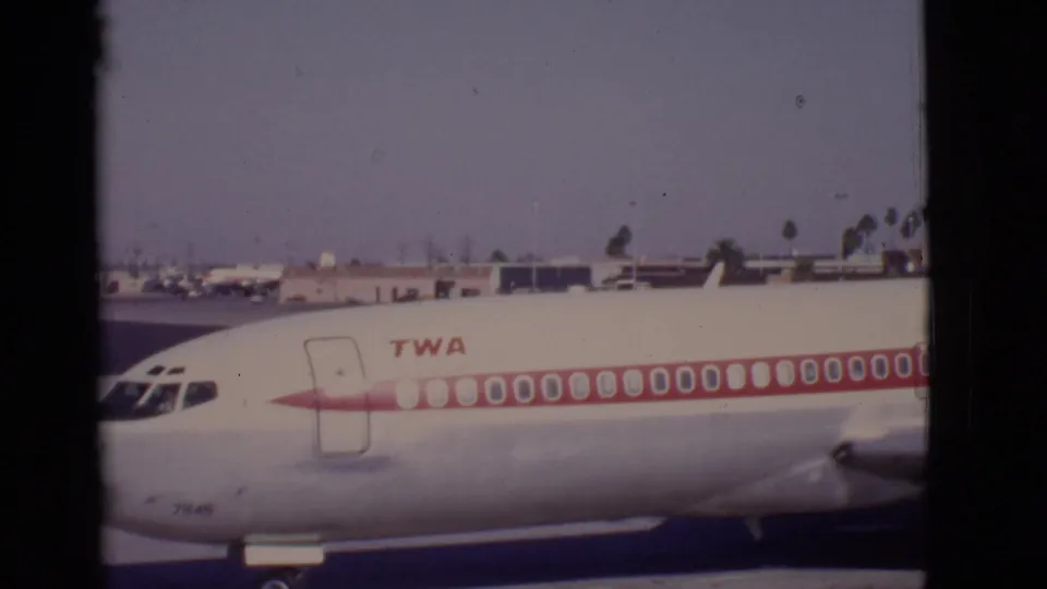 1968 Arizona airport side view of a parked TWA airliner, showing the red stripe, logo, windows, and background ramp structures.